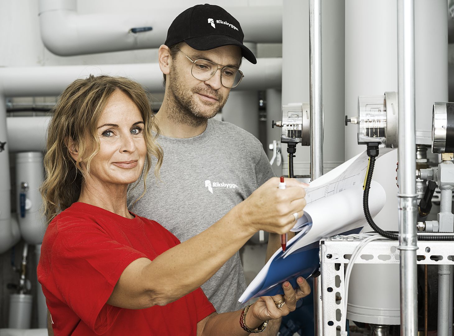 Två personer diskuterar vid teknisk utrustning med rör och mätare, och håller ett papper med anteckningar