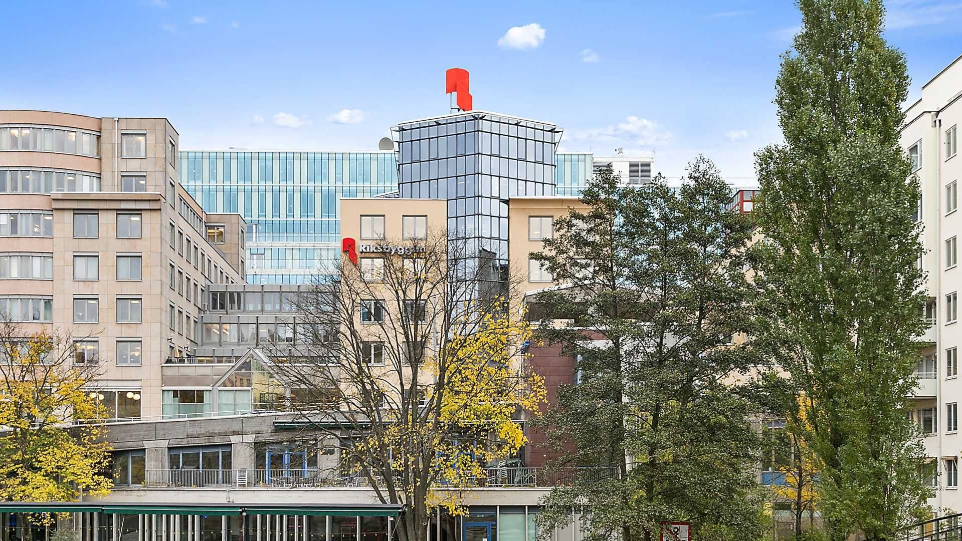 Modern kontorsbyggnader med glasfasader omgivna av träd under en klarblå himmel